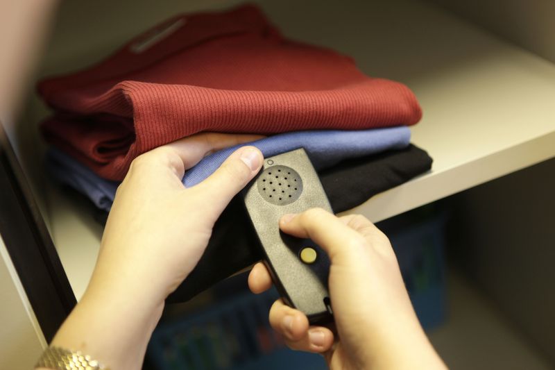 Ein Farberkennungsgerät, ein schwarzes Gerät, etwas kleiner als eine Fernbedienung, wird an einen violetten Pullover gehalten, der auf einem Regal liegt.