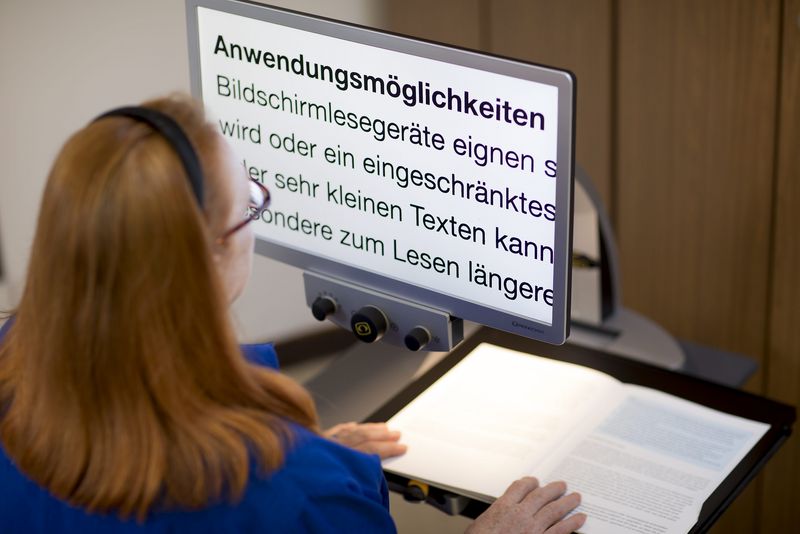 Eine Frau nutzt ein Bildschirmlesegerät. Das Buch liegt auf einer Platte, die Schrift wird vergrößert auf einem Bildschirm angezeigt.