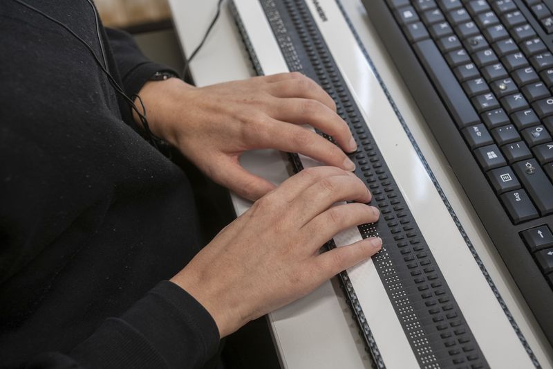 Eine Braillezeile unter einer Computertastatur, zwei Hände liegen auf der Zeile.